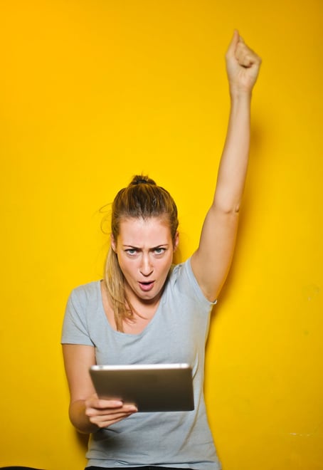 Whooo hooo. Excited woman holding a tablet in front of a yellow wall